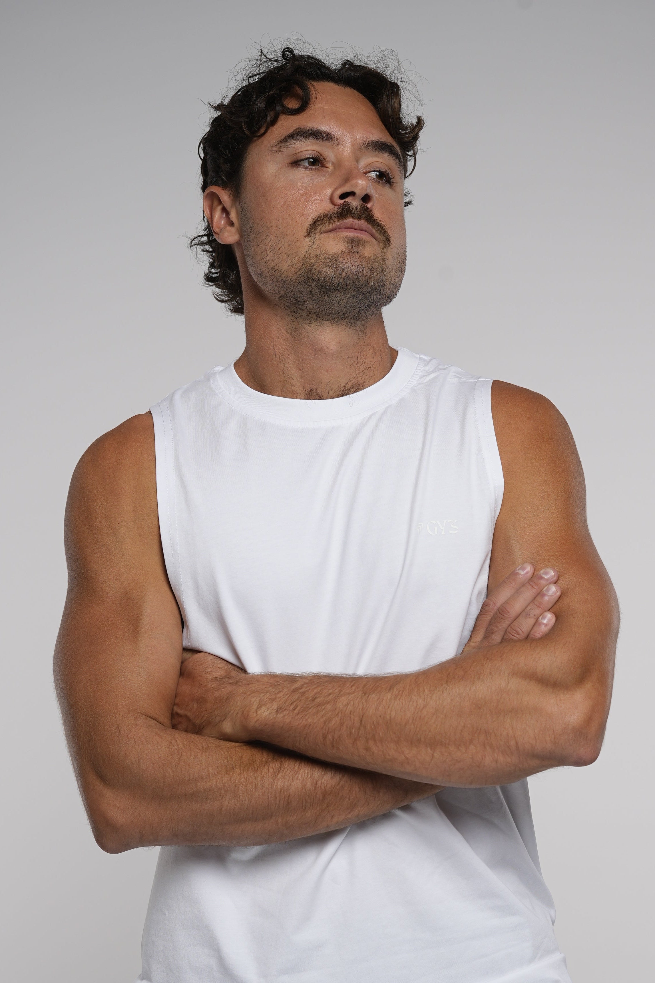 Man wearing a white tank top and black pants on a plain background